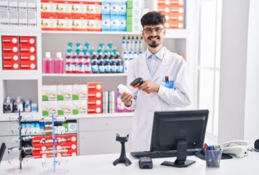 Young hispanic man pharmacist smiling confident scanning pills bottle at pharmacy
